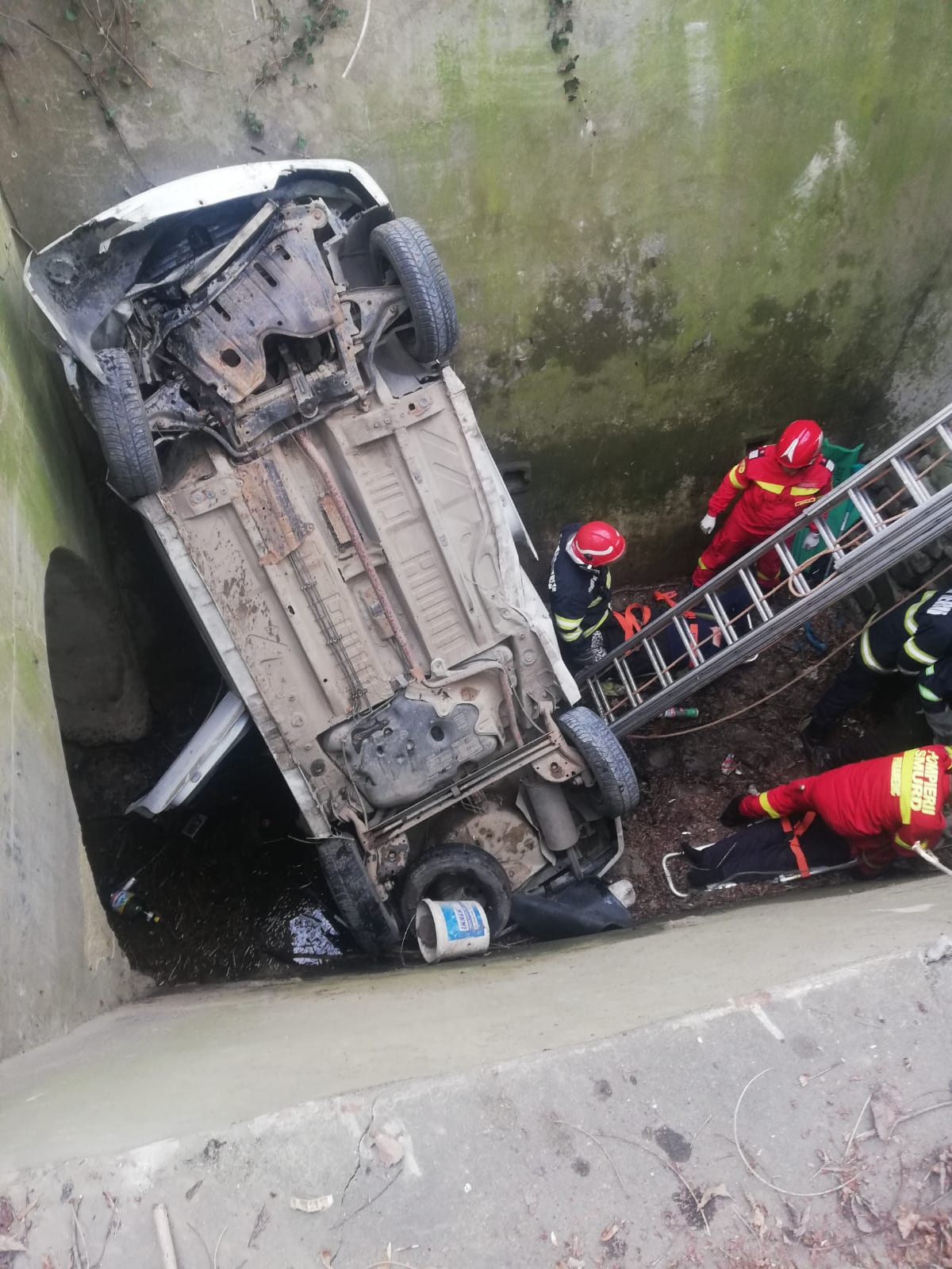 Autoturism căzut într-un canal adânc. Doi bătrâni, soț și soție, au rămas blocați